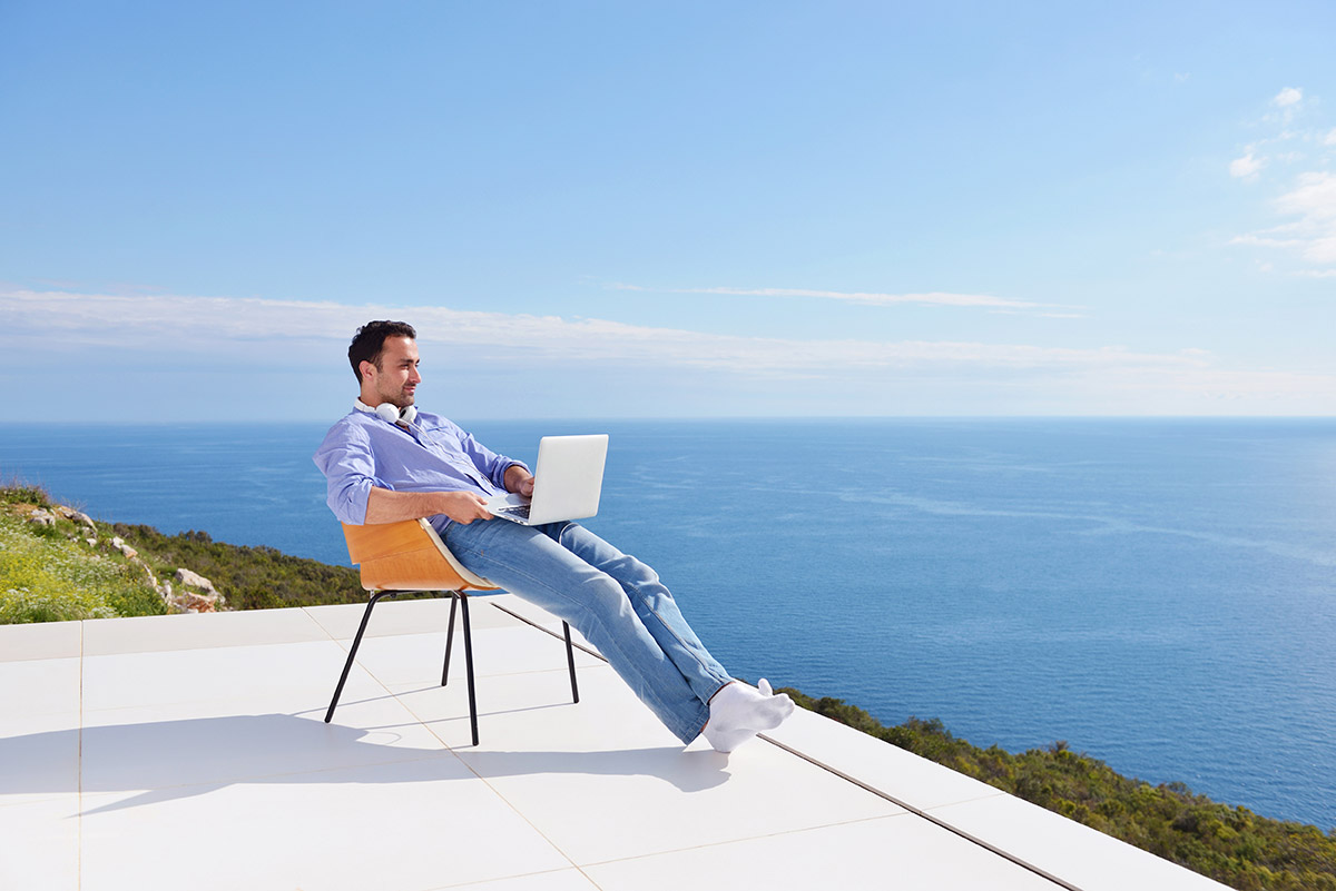 Man sitting on terrace with laptop looking out to sea