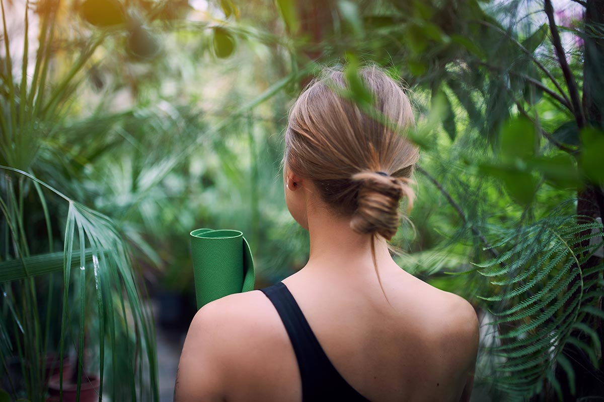 Girl from behing carrying a green Yoga mat