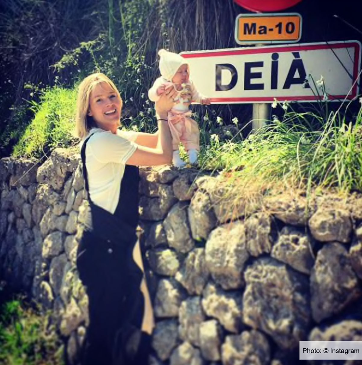 Lady holding baby up to Deia village sign in Mallorca