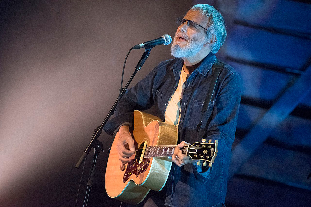 Yusef/Cat Stevens with acoustic guitar on stage.