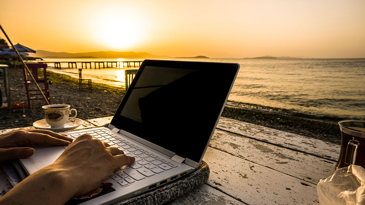 working on laptop on table by the sea at sunset.