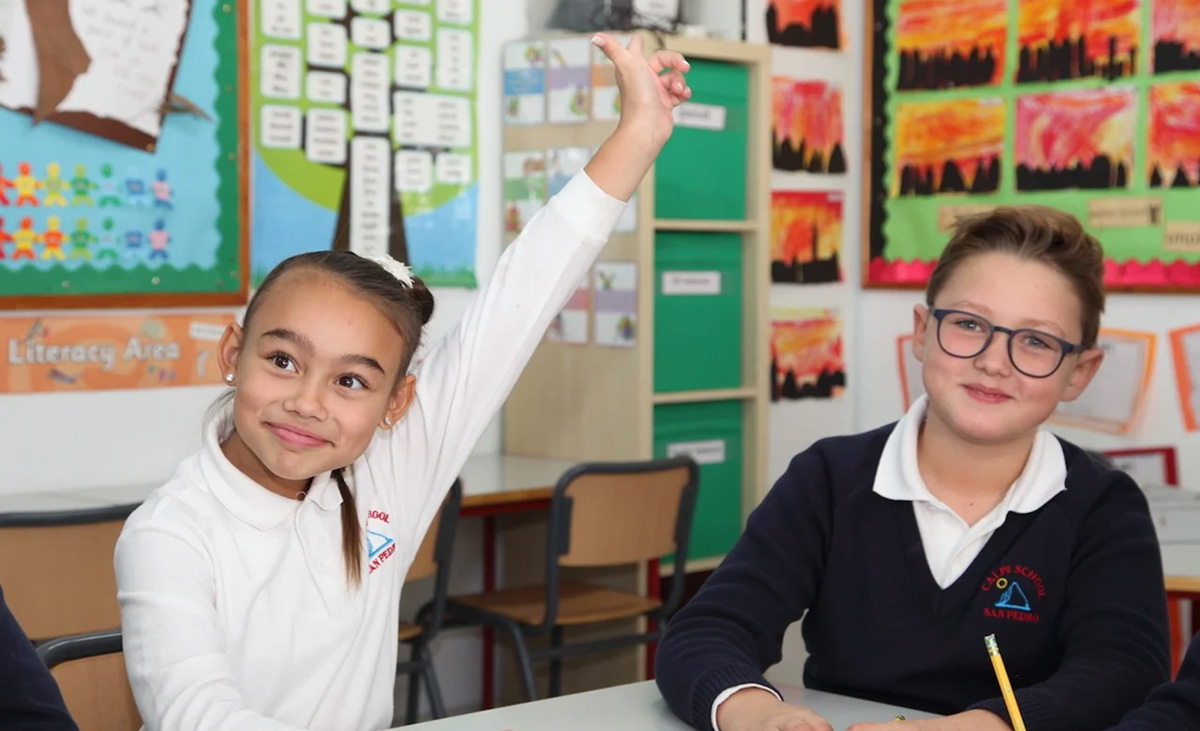 Two happy children raising hands in school classroom