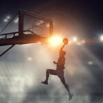 Basketball player dripping the ball in the net under floodlight.