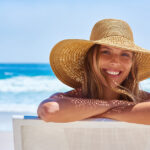 Girl on beach with floppy hat. Blue sea behind