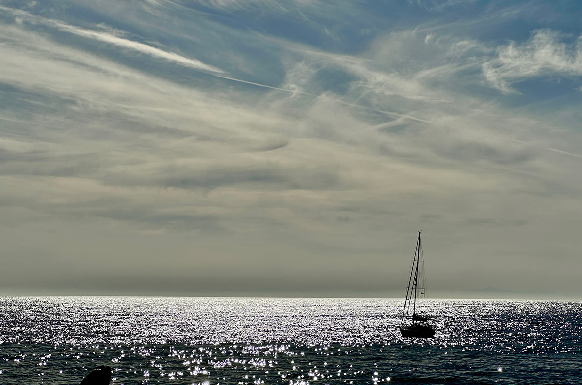 Yacht on glistening sea with wispy clouds on the horizon