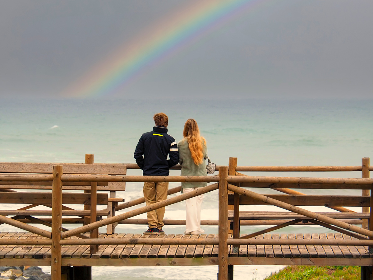 Couple looking at rainbow out to sea.